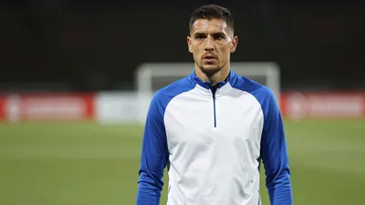 Mid-30s anonymous Gent striker, athletic build, waist-up, face sharp and centered, wearing a plain blue and white...