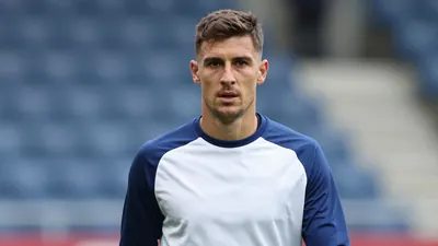 Mid-30s Gent midfielder, athletic build, waist-up, intense gaze, wearing a plain blue and white training top (solid navy...