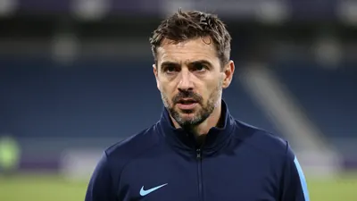A focused Gent coach in a navy blue tracksuit, mid-speech during a post-match interview
