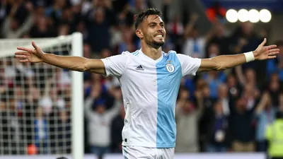 A photo of Tiago Araujo celebrating a volley goal with the Gent fans in the background, with a floodlight rim light and...
