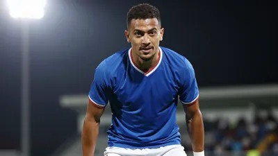 A photorealistic image of a young Gent player, aged 20-25, with a rugged build, wearing a blue jersey and white shorts...