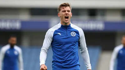 A determined, athletic 25-year-old Gent defender, wearing a plain blue and white training top, celebrates with intense...