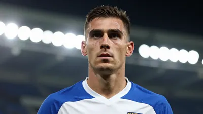 A mid-30s anonymous male forward in a solid blue and white kit, head-and-shoulders, looking determined, background...