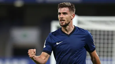 A focused mid-20s male footballer in a solid dark blue jersey, athletic build, celebrating a goal with a clenched fist