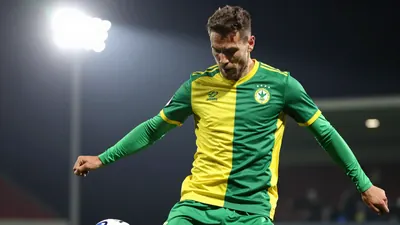 A photorealistic image of a Gent player, in action, kicking the ball, with the player's face visible, and the background...